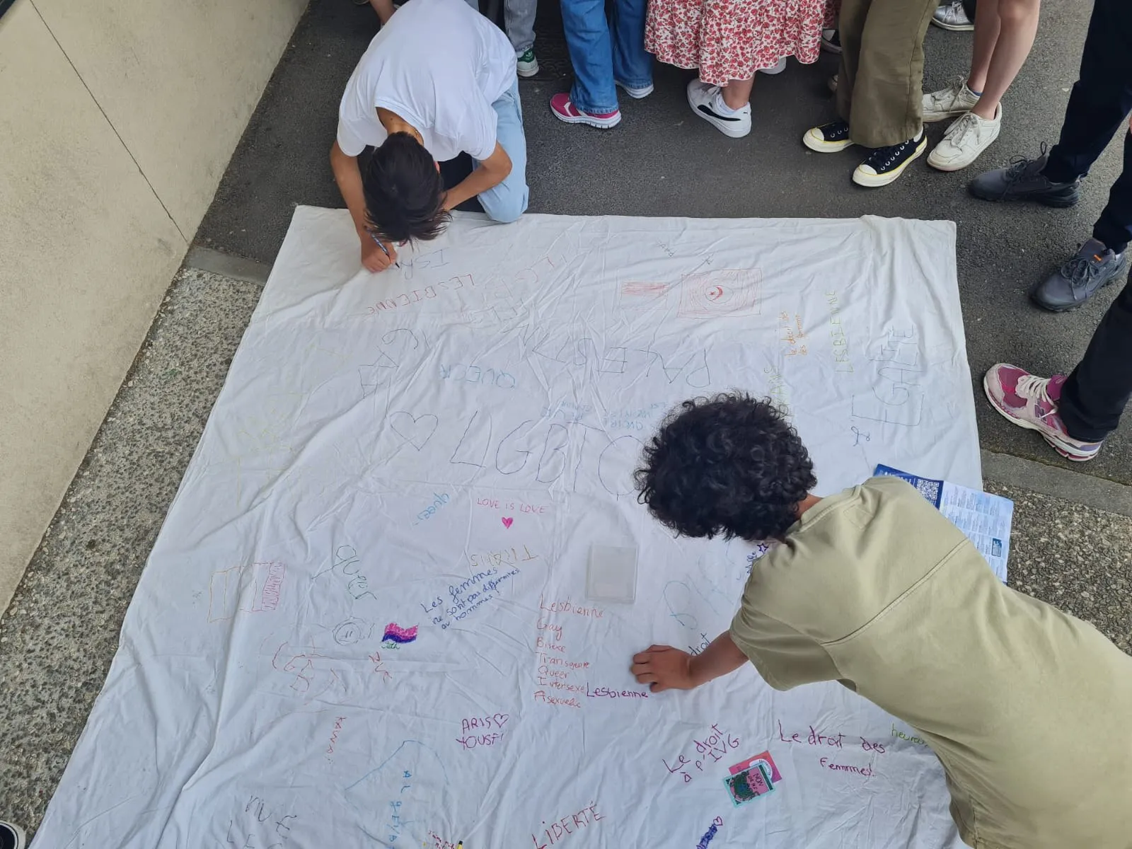 Des élèves écrivent des messages sur une grande banderole au sol