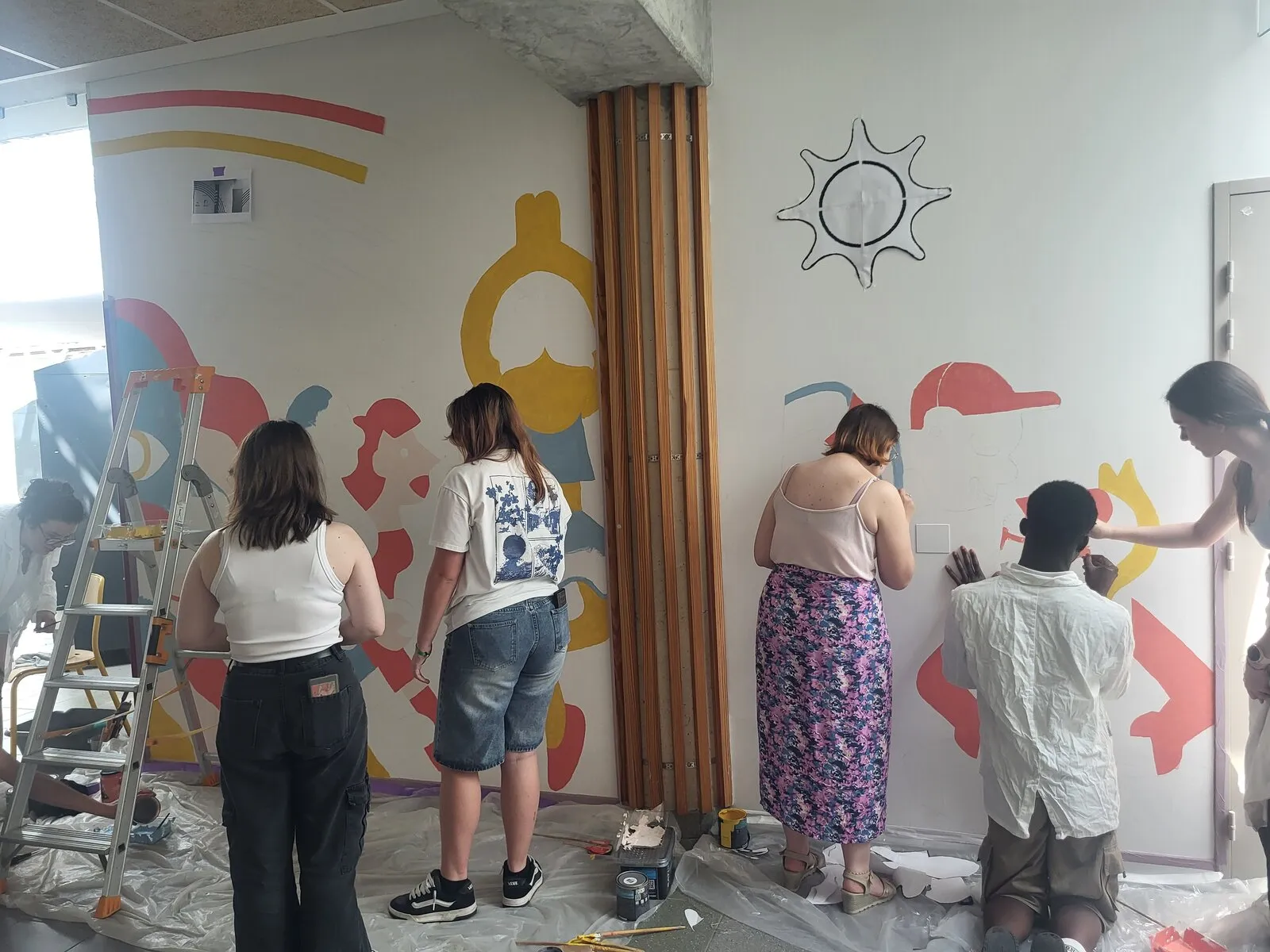 Des élèves de dos peignent une grande fresque colorée sur un mur de leur établissement